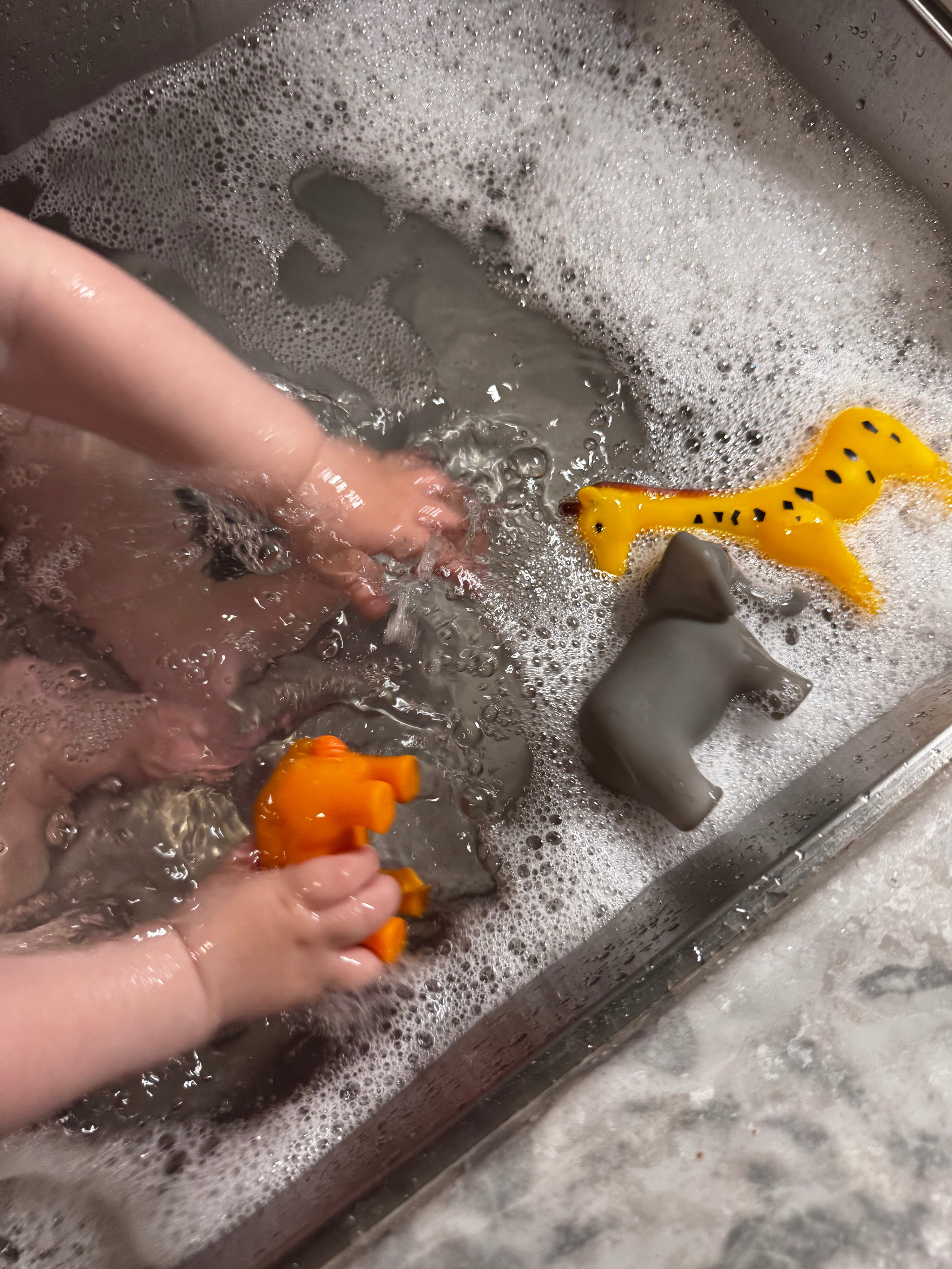 Baby playing with animal toys and taking a bath in the sink.